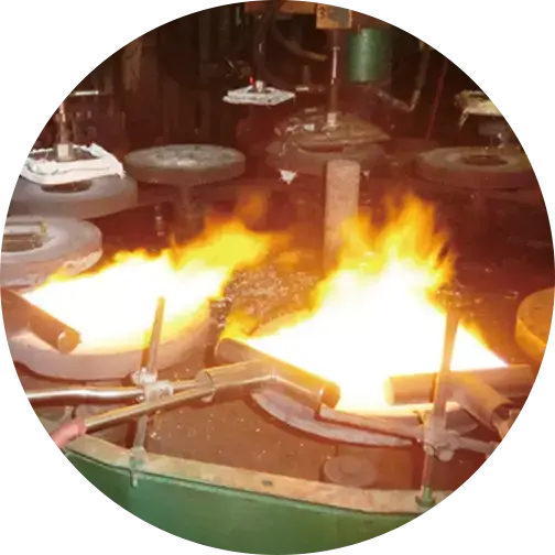 Close-up of industrial glass blowing process with intense open flames and machinery, indicating high-temperature production environment.