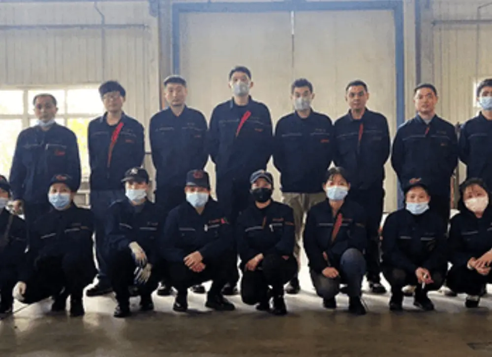 A group of workers wearing matching uniforms and safety gear posing in a factory environment.