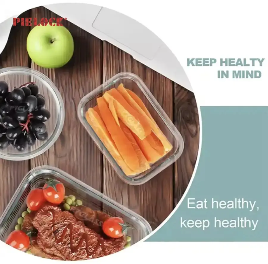 Glass food containers with fresh produce including carrot sticks, grapes, and a meal with a steak and cherry tomatoes. Green apple nearby.